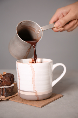 Woman pouring hot chocolate from cezve into cup on grey tableの写真素材