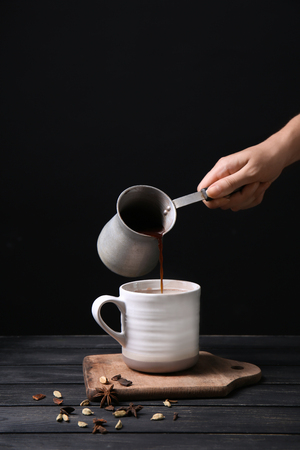 Woman pouring hot chocolate from cezve into cup on wooden tableの写真素材