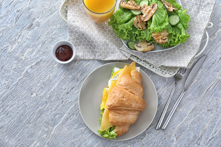 Plate with tasty croissant sandwich and fresh salad on light table