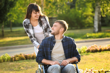 Young man in wheelchair and his wife outdoorsの写真素材