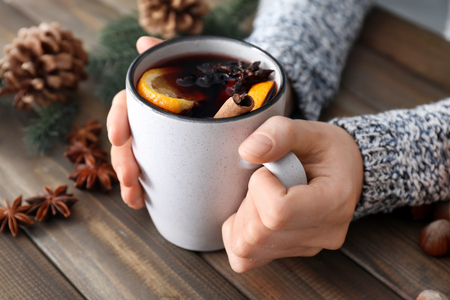 Woman holding cup of delicious mulled wine at wooden table, closeupの写真素材