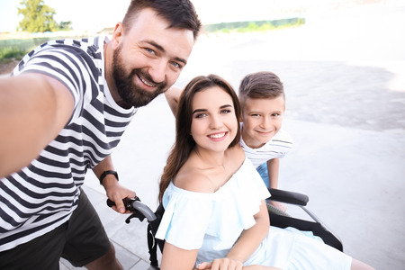 Young woman in wheelchair with her family taking selfie outdoorsの写真素材