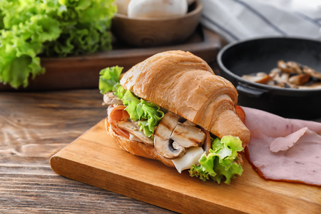 Tasty croissant sandwich with mushrooms on wooden boardの写真素材