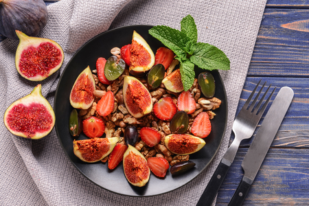 Plate with tasty fruit salad and nuts on color wooden tableの写真素材