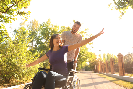 Happy young woman in wheelchair and her husband outdoorsの写真素材