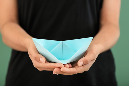 Woman holding origami boat on color background, closeup