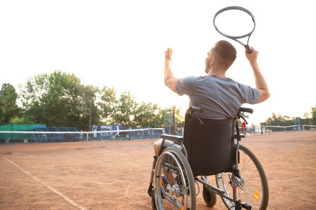 Young man in wheelchair playing tennis on courtの写真素材