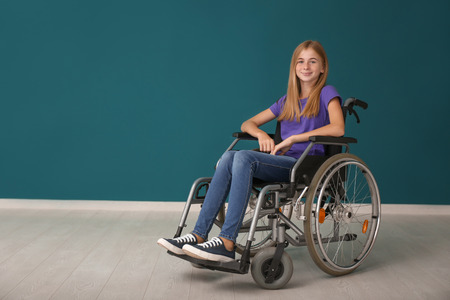 Teenage girl in wheelchair against color wall