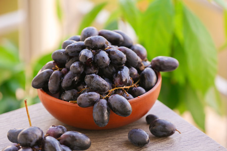Bowl with sweet grapes on wooden table outdoors