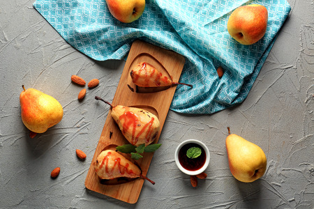 Wooden board with tasty baked pears and syrup on grey tableの写真素材