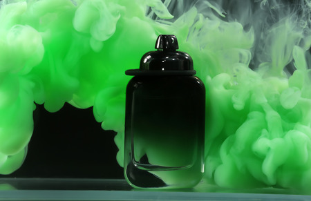 Bottle of perfume in color smoke on dark background