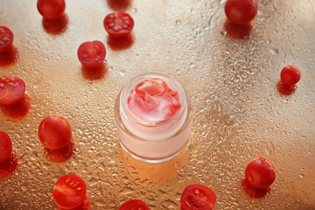 Jar with body cream and tomatoes on golden table