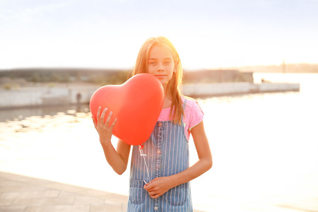 Cute little girl with heart-shaped air balloon near riverの写真素材
