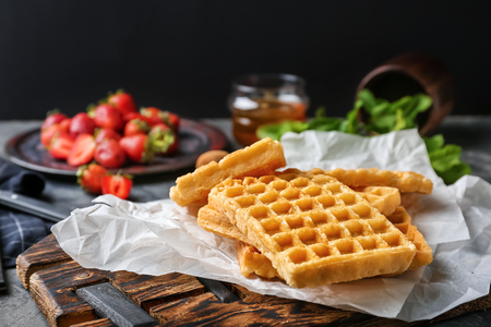 Wooden board with delicious Belgian waffles on tableの写真素材