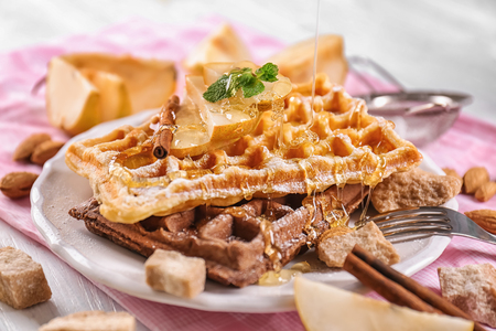 Pouring of honey onto delicious waffles with pear slices on plateの写真素材