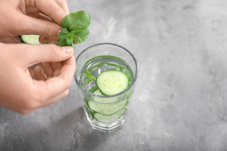 Woman putting mint into glass with cucumber water on grey table, closeupの写真素材