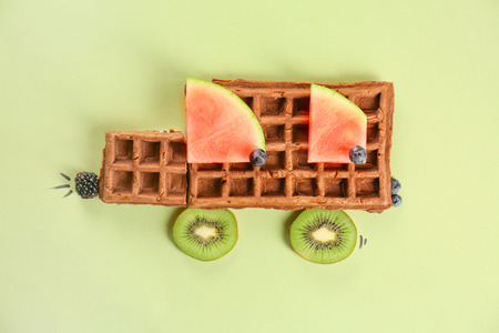 Creative composition with delicious waffles and fruits on color background