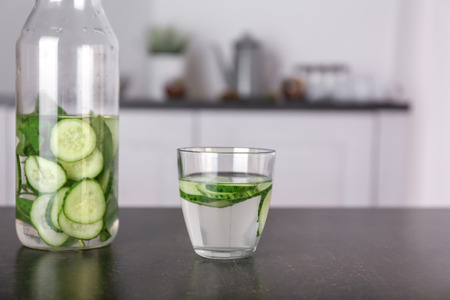 Glass and bottle with tasty fresh cucumber water on dark tableの写真素材