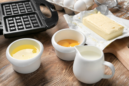 Ingredients with modern waffle maker on wooden tableの写真素材