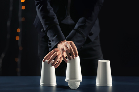 Magician showing tricks with cups on dark backgroundの写真素材