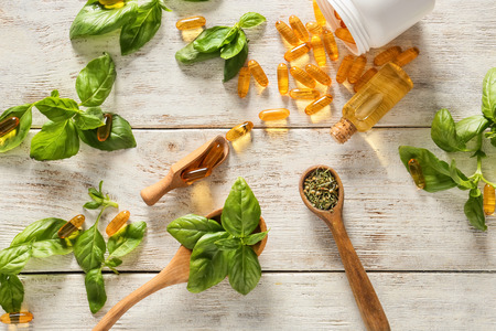 Fresh basil leaves with capsules and essential oil on wooden tableの写真素材