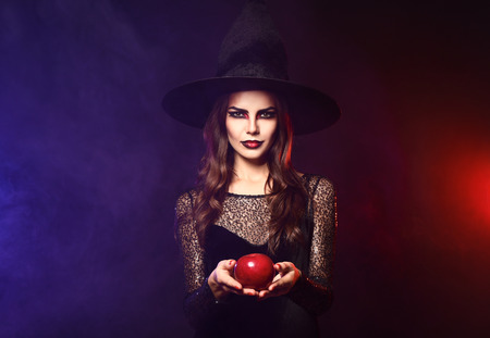 Beautiful woman dressed as witch for Halloween with apple on dark color backgroundの写真素材
