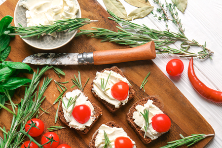 Tasty sandwiches with spread, tomatoes and herbs on wooden board, top viewの写真素材