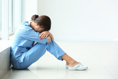 Tired female nurse sitting on floor in hospitalの写真素材