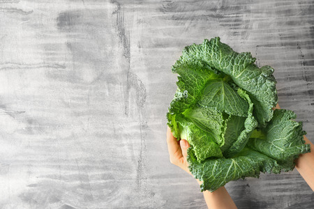 Woman holding fresh savoy cabbage on grey backgroundの写真素材