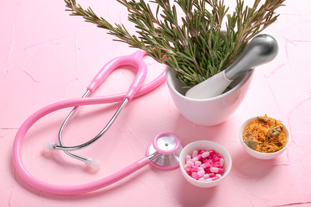 Mortar with fresh rosemary, capsules, flowers and stethoscope on color tableの写真素材