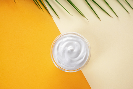 Jar with body cream and tropical leaf on color backgroundの写真素材