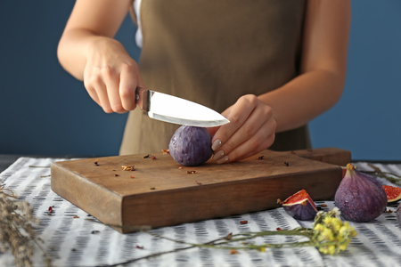 Woman cutting fresh ripe fig at tableの写真素材