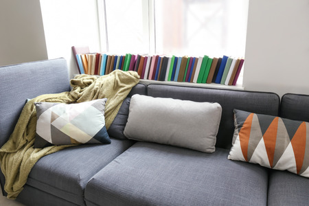 Cozy sofa with soft plaid and pillows near window in roomの写真素材