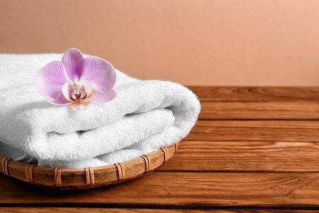 Wicker tray with clean soft towel and flower on wooden tableの写真素材