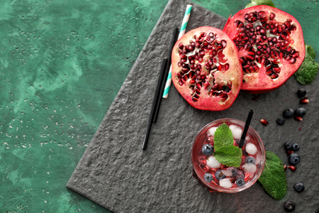 Glass with delicious summer cocktail and cut pomegranate on tableの写真素材