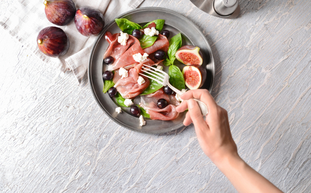 Woman eating delicious fig salad on light backgroundの写真素材
