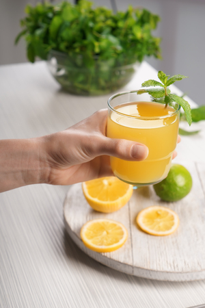 Woman holding glass of fresh lemon juice over tableの写真素材