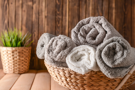 Wicker basket with rolled clean soft towels on wooden tableの写真素材