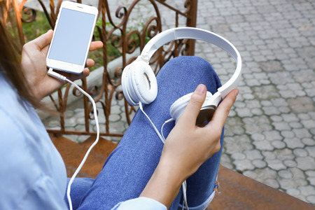 Young woman with mobile phone and headphones sitting on stairs outdoors
