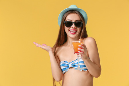 Beautiful woman in swimming suit and with tasty summer cocktail on color backgroundの写真素材