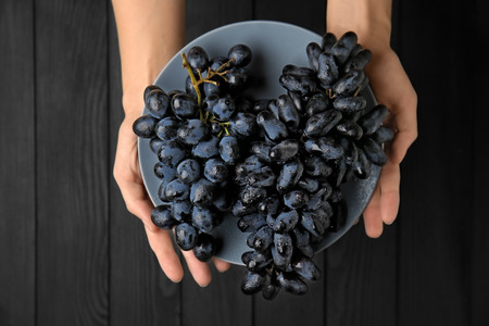 Woman holding plate with fresh ripe juicy grapes on dark wooden backgroundの写真素材