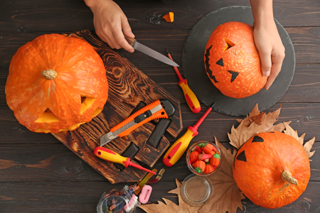 Woman making jack-o-lantern for Halloween party on wooden tableの写真素材