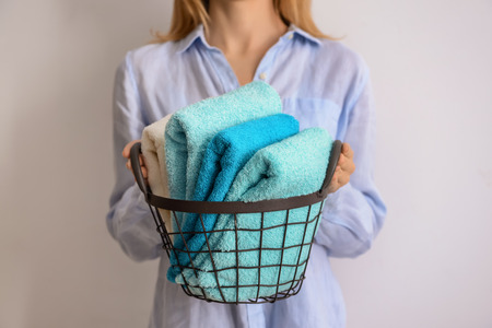 Woman holding metal basket with clean soft towels on light backgroundの写真素材