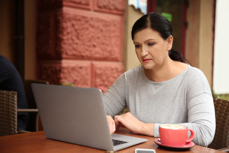 Beautiful mature woman working on laptop in cafeの写真素材