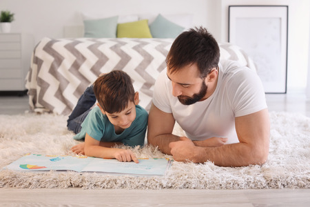 Cute little boy and his father reading book at homeの写真素材