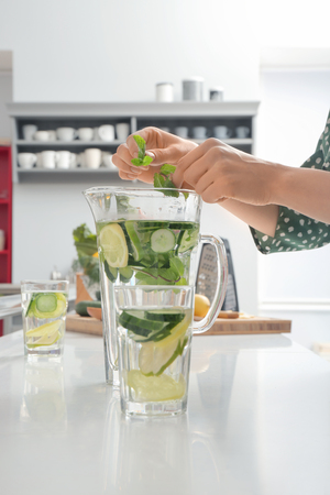 Woman preparing fresh cucumber water in kitchenの写真素材