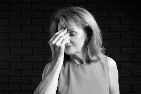 Black and white portrait of mature woman suffering from headache on dark backgroundの写真素材