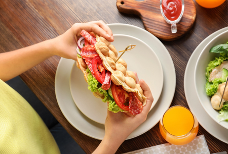 Woman eating delicious bubble waffle on wooden tableの写真素材
