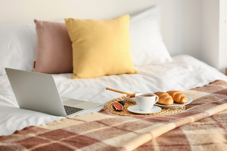 Wicker mat with delicious breakfast and laptop on bedの写真素材