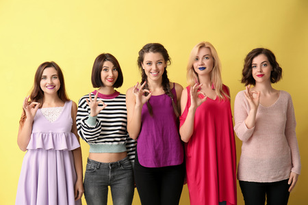 Portrait of beautiful women showing OK gesture on color backgroundの写真素材